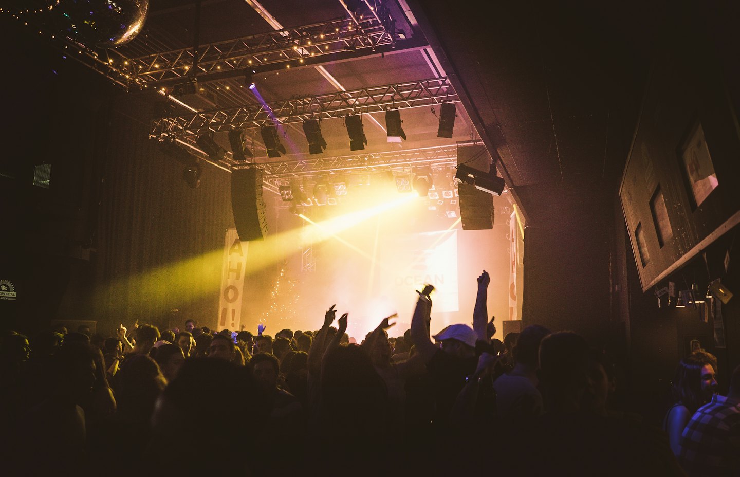 Concert audience with hands raised facing the illuminated stage.