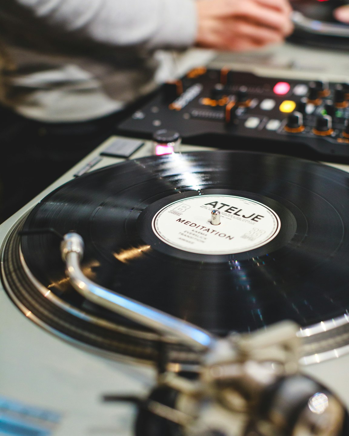Hands operating DJ mixer with vinyl record spinning.
