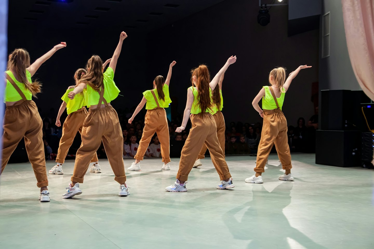 Dancers in neon yellow tops and brown overalls on stage.