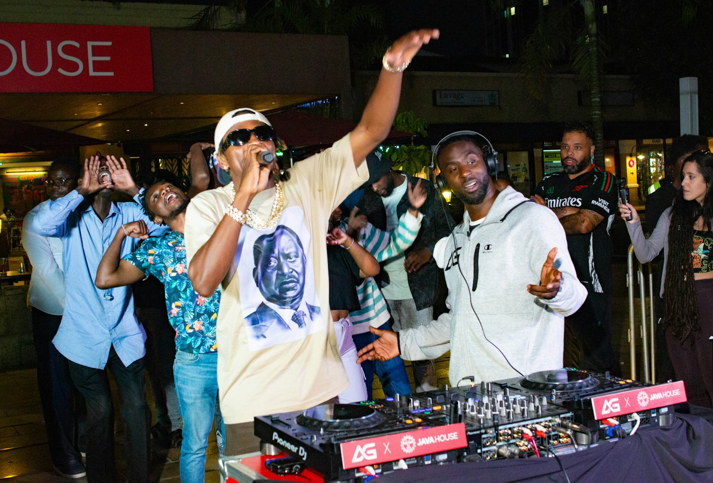 A performer and DJ entertain a crowd at an outdoor concert.