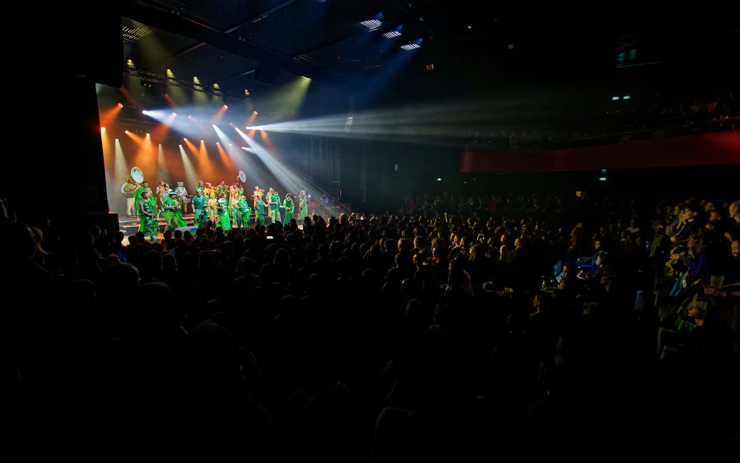 Performers in green costumes dancing on a stage for an audience.