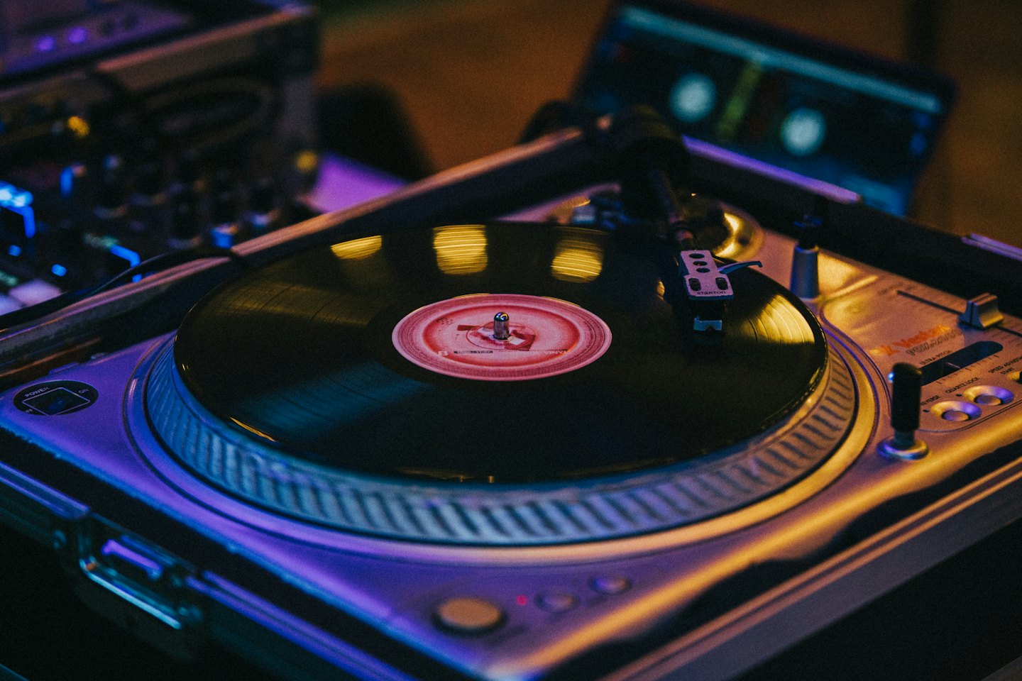 Black vinyl record spinning on a silver turntable with purple lighting.